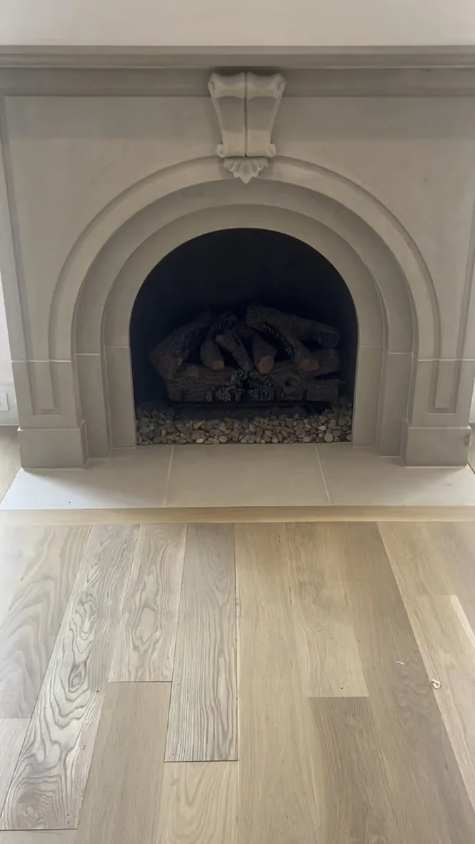 Traditional arched fireplace with a light stone surround and gas logs.